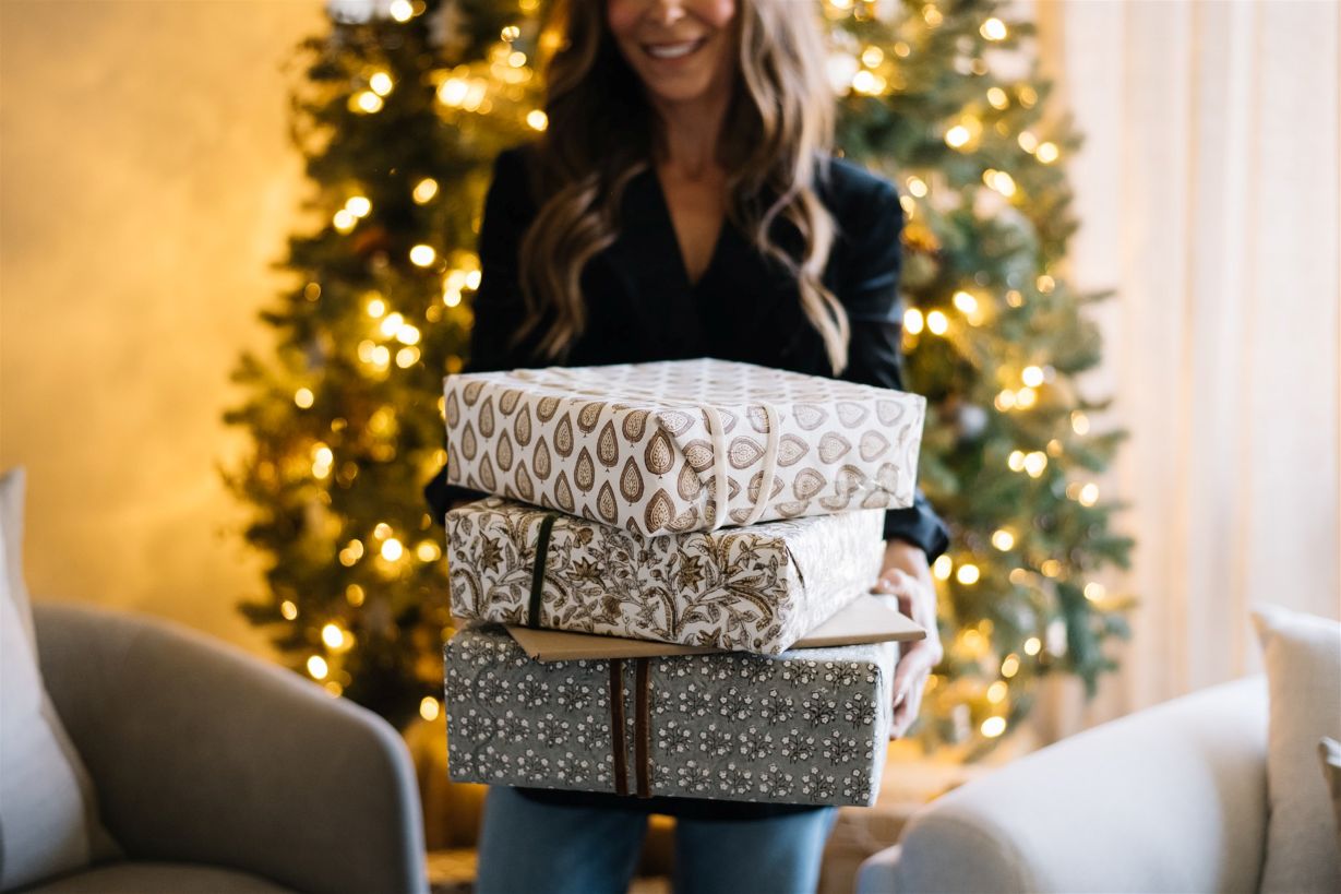 a woman with Christmas gifts wrapped  standing in front of decorated Christmas tree
