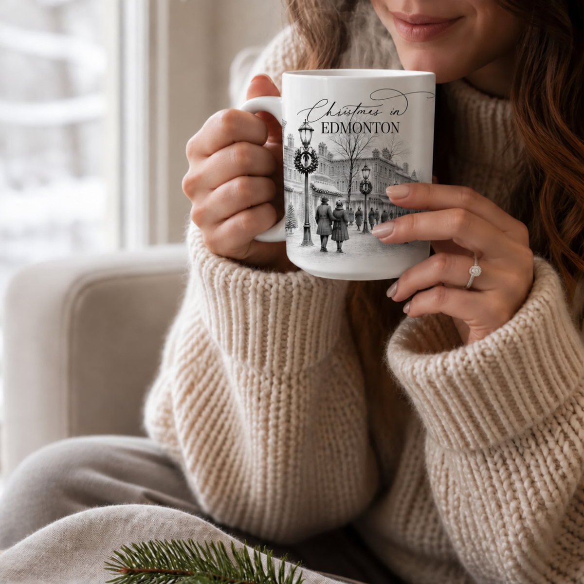 Woman in a cream knit sweater holding a Christmas in Edmonton mug with a festive town illustration beside a window.