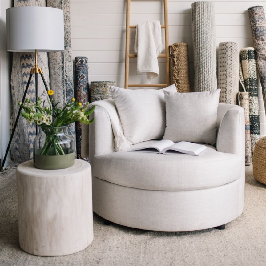 White cuddle chair with a side table and lamp in a room with textured wall coverings in St. Albert.