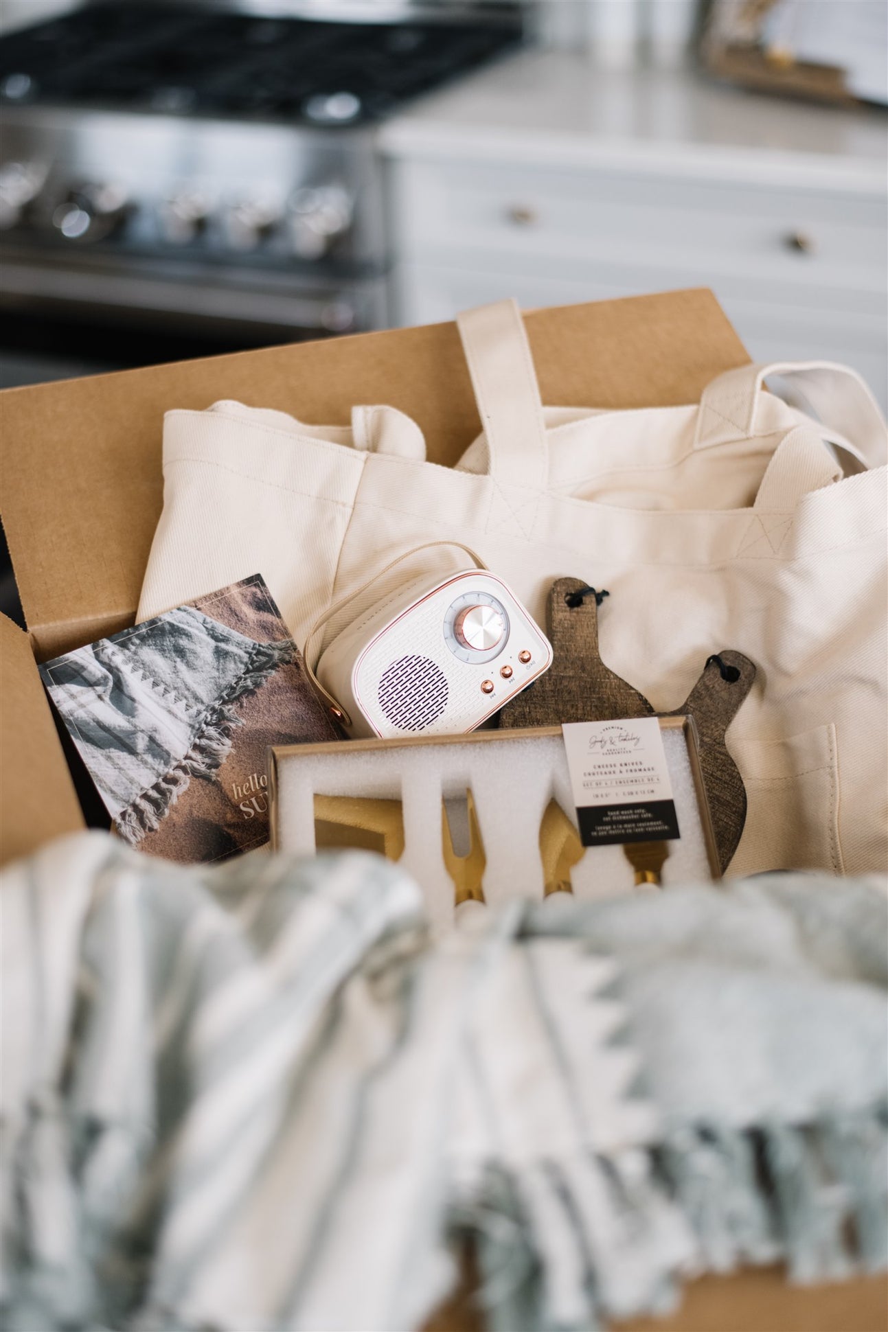 Box containing a white electronic device, a plush toy, and a blanket on a kitchen counter.